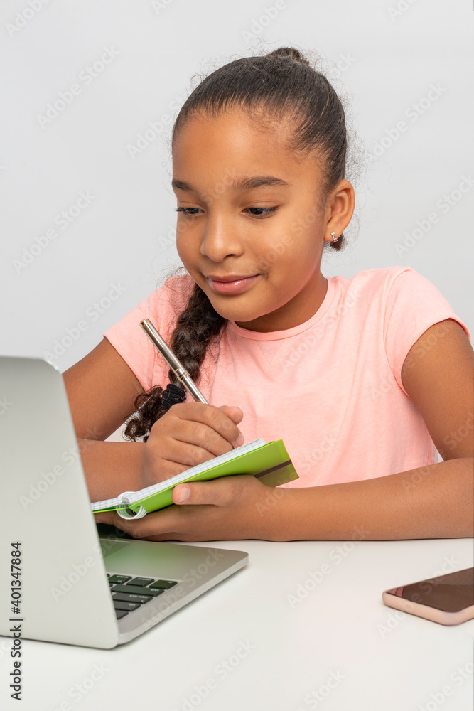 Portrait of the schoolgirl siting at the table indoors and doing her homework Portrait of the schoolgirl siting at the table indoors and doing her homework