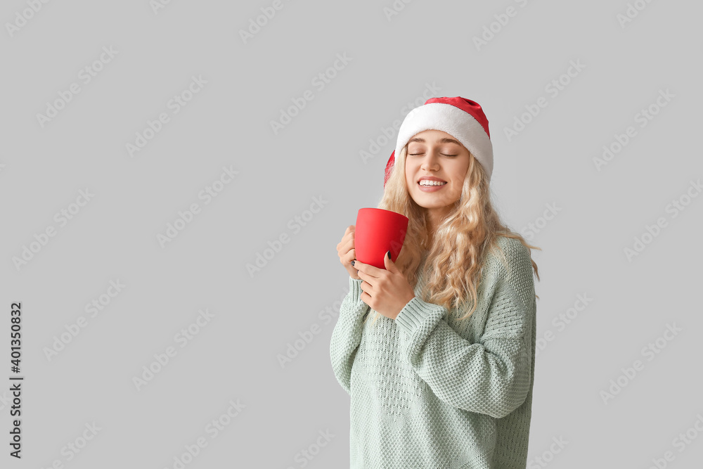 Beautiful young woman in Santa hat with cup on light background Beautiful young woman in Santa hat with cup on light background
