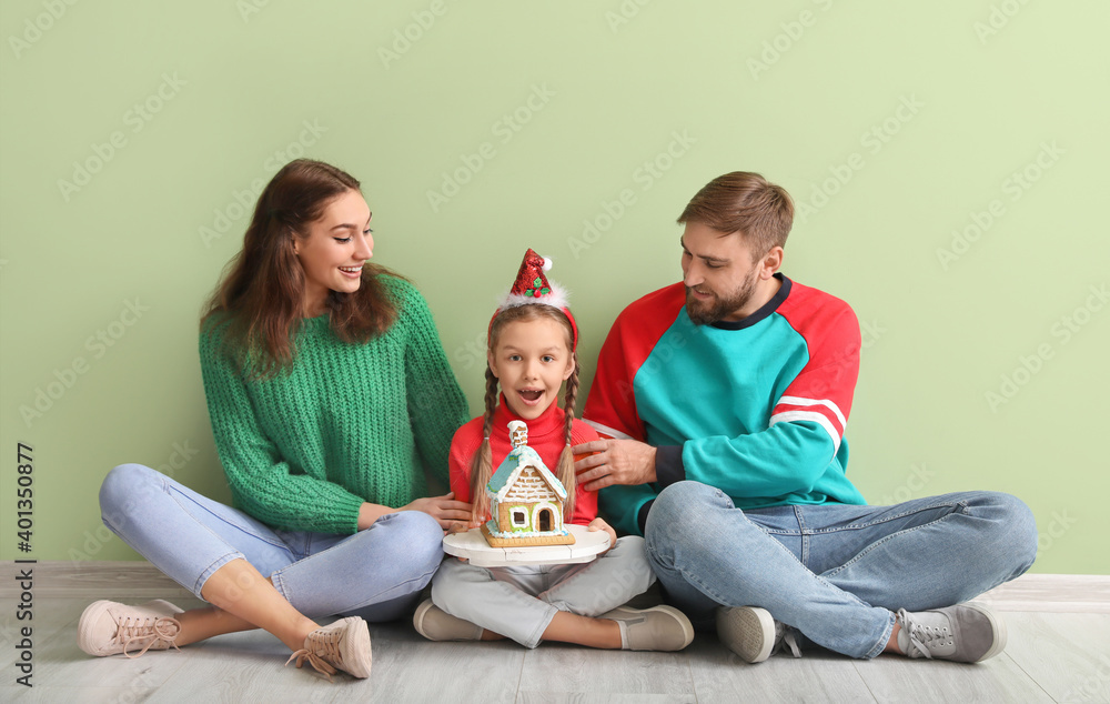 Happy family with gingerbread house sitting near color wall. Christmas celebration