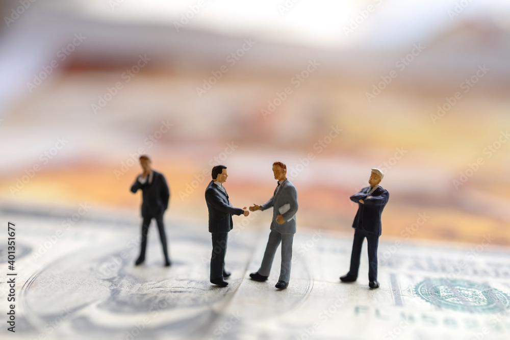 Miniature people: Businessman handshake with money on world map, Investment, agreement, partnership and business concept Miniature people: Businessman handshake with money on world map, Investment, agreement, partnership and business concept