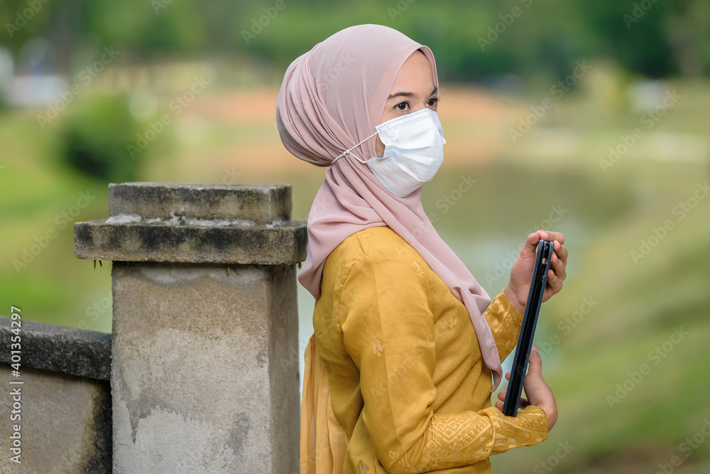 Asian muslim student woman with traditional dress wearing medical face mask at le lake