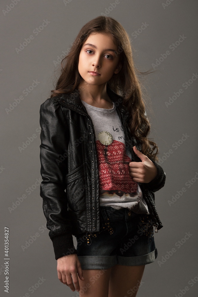 beautiful girl in denim shorts and a leather jacket posing in the studio on a gray background beautiful girl in denim shorts and a leather jacket posing in the studio on a gray background