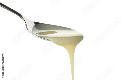 Spoon with dripping condensed milk isolated on white background