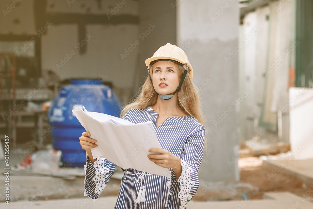 Focused young woman engineer in a helmet is thinking about developing a plan for building a dwalling, portrait