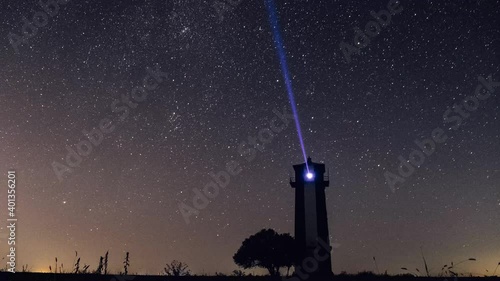 4K. Timelapse of beautiful night landscape with lighthouse over starry sky as a background