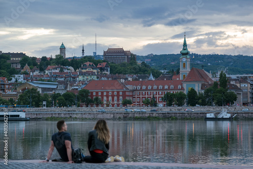 Photography Unfocused couple sitting by the river against old city in dusk