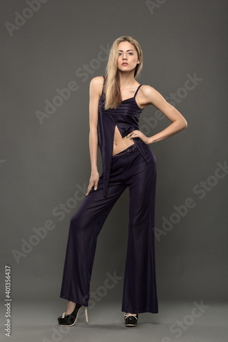 Blonde girl in black pants posing in the studio on a gray background