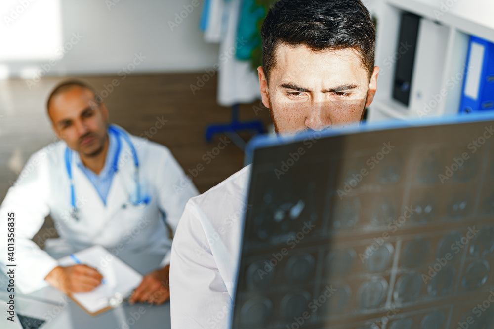Fototapeta premium Two male doctors examine MRI brain scan of a patient in cabinet