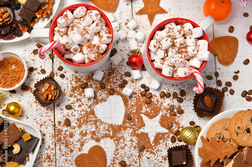 sweet food top view background for merry christmas or new year holiday decoration - chocolate candies, tangerines, cookies, marshmallow and cocoa latte on white wood