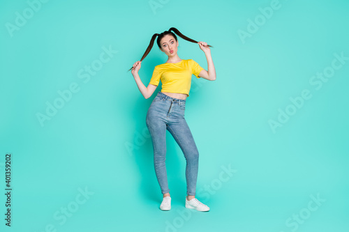Full size photo of optimistic funny brunette girl blow kiss stand wear yellow t-shirt jeans sneakers isolated on blue color background
