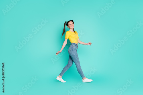 Full size profile photo of optimistic nice brunette girl go wear yellow t-shirt jeans sneakers isolated on blue color background