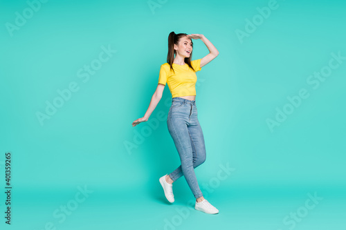 Full size profile photo of optimistic brunette girl go see wear yellow t-shirt jeans sneakers isolated on cyan color background