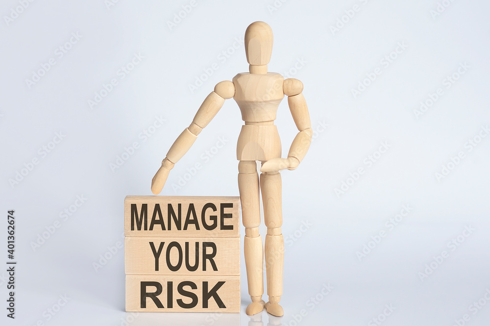 Wooden man shows with a hand text MANAGE YOUR RISK concept on the wooden block Wooden man shows with a hand text MANAGE YOUR RISK concept on the wooden block