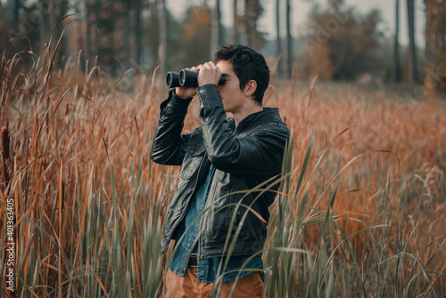 young man with binoculars looks into the distance on the background of nature
