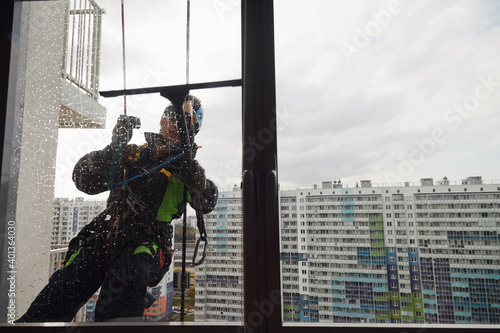 Industrial mountaineering worker hangs over residential building while washing exterior facade glazing. Rope access laborer hangs on wall of house. Concept of urban works. Copy space