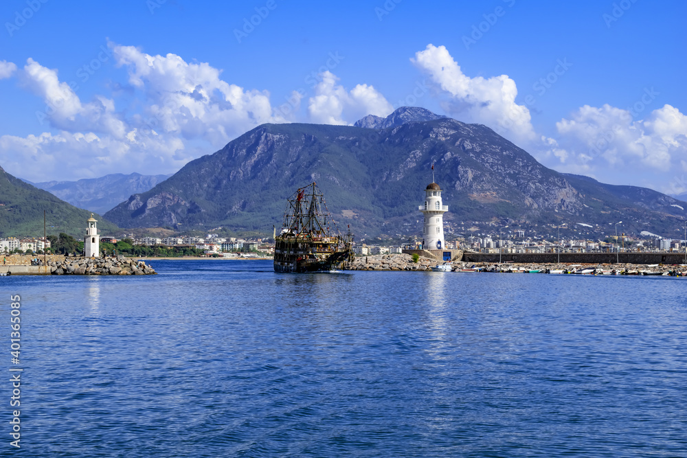 A large pirate ship enters the port between two lighthouses in Alanya (Turkey). Beautiful seascape of the bay in the resort town of the Turkish Riviera
