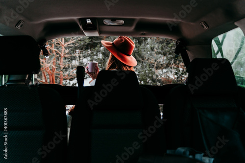 back view from inside a car of young woman outdoors wearing stylish hat. Winter season. snowy mountain background © Eva