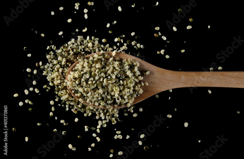 Peeled hemp seed with wooden spoon isolated on black background, top view