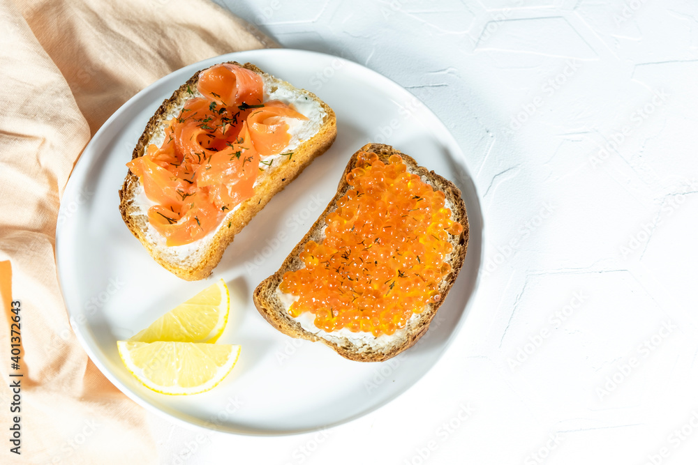 Slices of bread with red caviar on plate on white background. red fish and arugula sandwich on a board, selective focus, copy space. Top view. Slices of bread with red caviar on plate on white background. red fish and arugula sandwich on a board, selective focus, copy space. Top view.