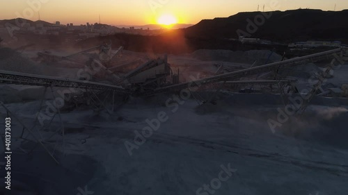 Flight forward above industrial landscape on outskirts of abstract city, mobile concrete batching plant station futuristic steel conveyors factory. Epic orange sunset. Postapacalypse cityscape dark photo