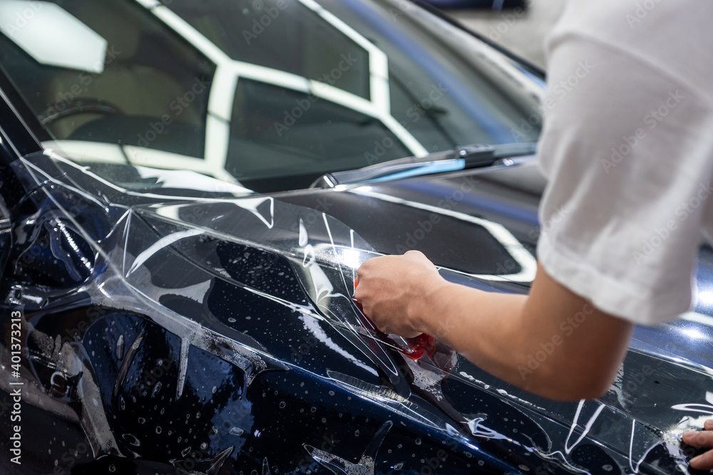 Car wrapping specialist cutting vinyl transparent film for protection car paint focus on hand holding cutting tools. Protective film. Car paint protection Car wrapping specialist cutting vinyl transparent film for protection car paint focus on hand holding cutting tools. Protective film. Car paint protection