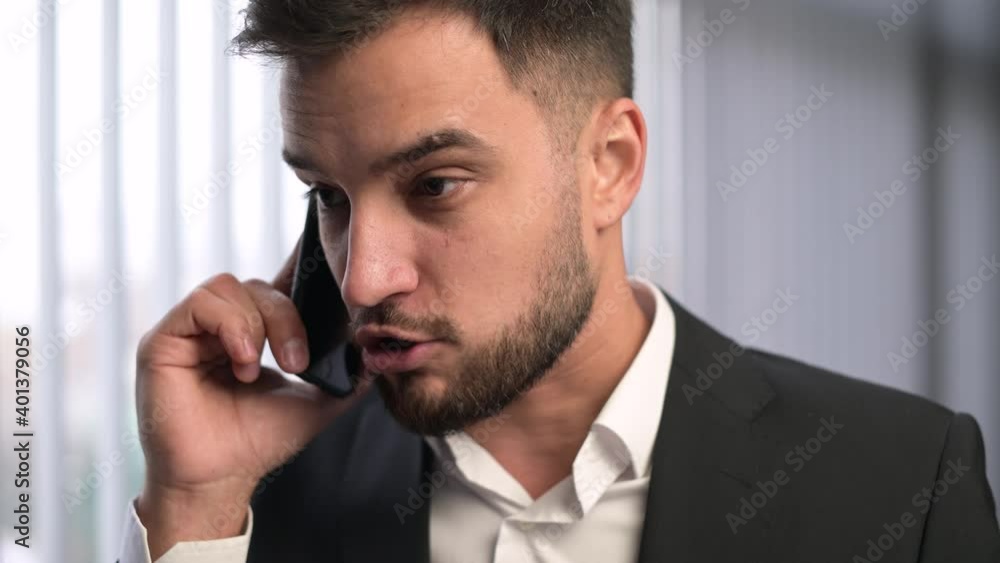 A young company executive speaks angrily on the phone, discussing bad reports. The man is angry and upset A young company executive speaks angrily on the phone, discussing bad reports. The man is angry and upset