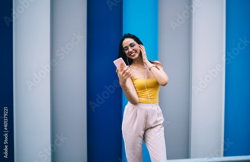 Prosperous hipster girl in glasses watching funny video connected to 4g on mobile gadget, joyful Caucaisan female youngster enjoying celular phoning and time for listening positive music songs