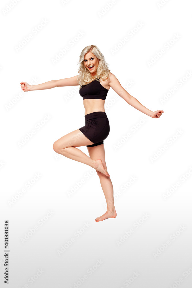 Portrait of a joyful fit young white female athlete with curly long blond hair posing by herself in a studio with a white background wearing black shorts & sports bra.