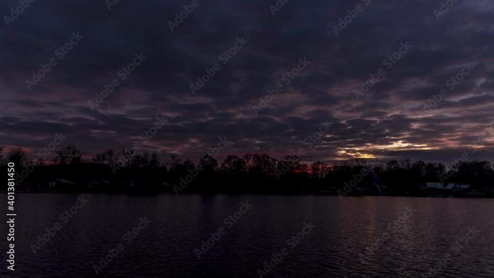 Timelapse of dark colored red and blue clouds moving fast above the lake during an autumn sunset in a landscape surrounded by trees. Timelapse of dark colored red and blue clouds moving fast above the lake during an autumn sunset in a landscape surrounded by trees.