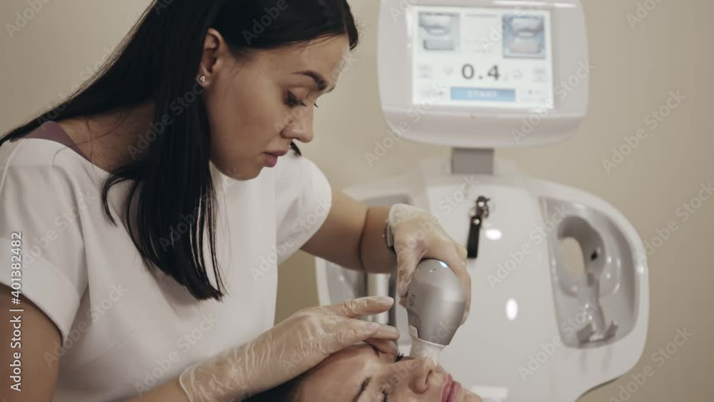 Cosmetologist in beauty office making lifting procedure on female patient with special device. Specialist moving along correction lines on woman face. Cosmetologist in beauty office making lifting procedure on female patient with special device. Specialist moving along correction lines on woman face.