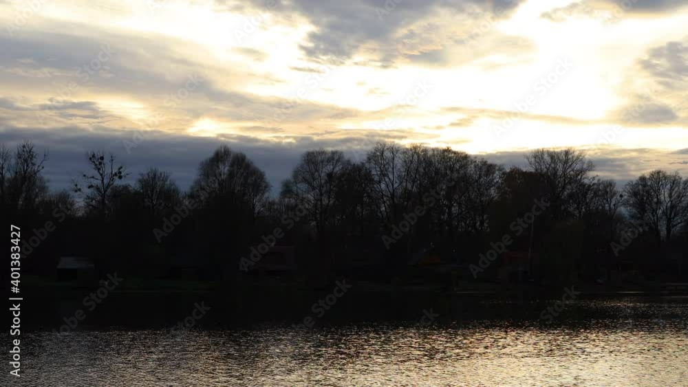 Timelapse of the lake surface during a colorful sunset where the surface reflects rays and a fast moving water surface with houses on the opposite side of the lake. Timelapse of the lake surface during a colorful sunset where the surface reflects rays and a fast moving water surface with houses on the opposite side of the lake.