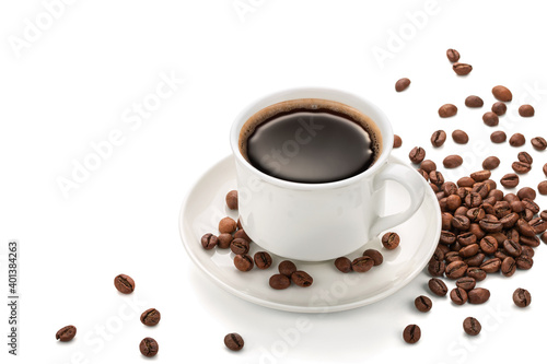 White cup with black coffee on a saucer with scattered coffee beans on a white background. Copy space.