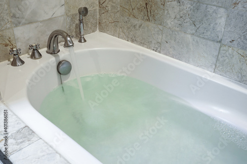 Stainless Faucet and turned on the water with a white bathtub in the bathroom.