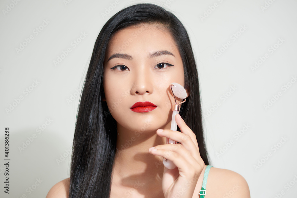 Face massage. Smiling woman using rose quartz facial roller for skin care, beauty treatment on white isolate background. Face massage. Smiling woman using rose quartz facial roller for skin care, beauty treatment on white isolate background.