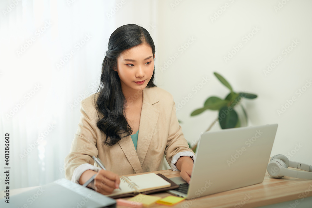 Image of young pleased happy cheerful cute beautiful business woman sit indoors in office using laptop computer Image of young pleased happy cheerful cute beautiful business woman sit indoors in office using laptop computer