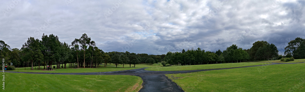 Beautiful panoramic morning view of a park with green grass, tall trees and dark cloudy sky, Fagan park, Galston, Sydney, New South Wales, Australia
