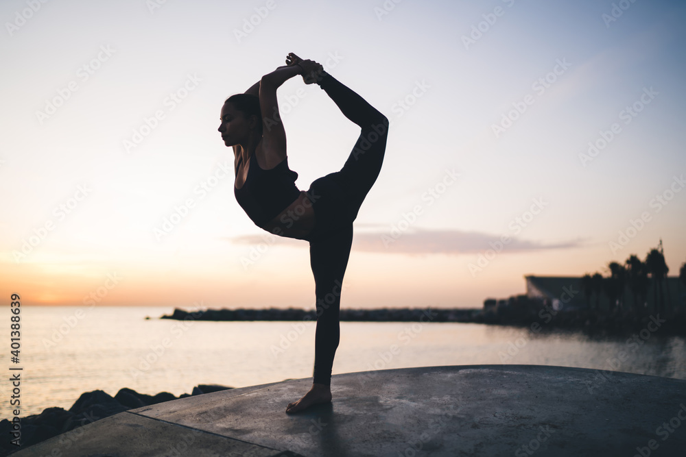 Flexible woman in tracksuit care about body stretching muscles during yoga meditation at coastline, female concentrated on thoughts training calmness and mental health wellness in retreat outdoors