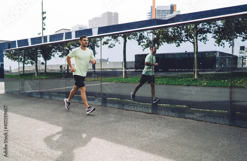 Motivated male jogger dressed in active wear running during morning time enjoying sportive lifestyle, good looking man in tracksuit have energetic cardio training for physical jogging at urbanity