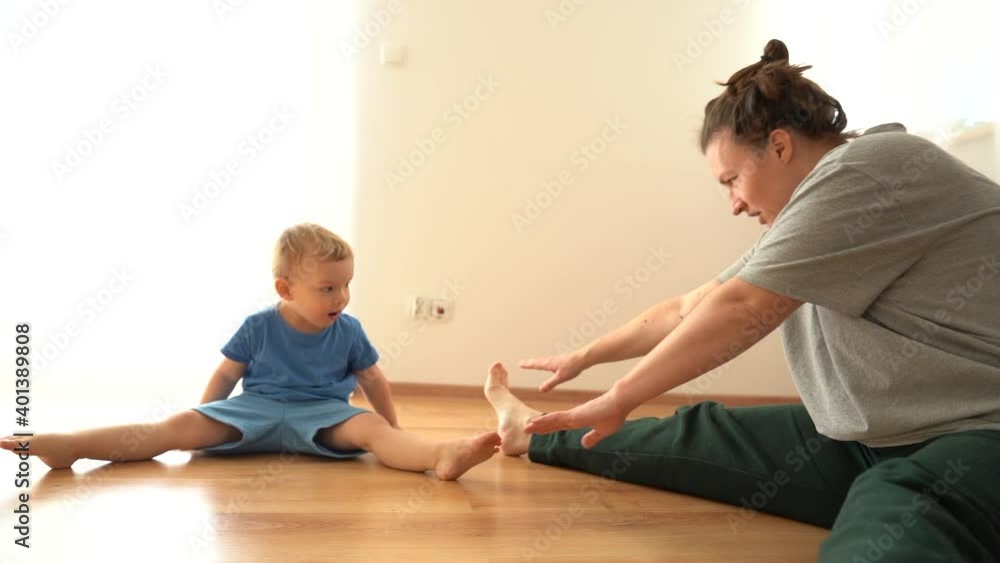 Hatha yoga fitness mother with baby. A young woman and her little son do gymnastics on the floor at home during a covid-19 lockdown. Stretching, funny video kid repeats after mom Hatha yoga fitness mother with baby. A young woman and her little son do gymnastics on the floor at home during a covid-19 lockdown. Stretching, funny video kid repeats after mom