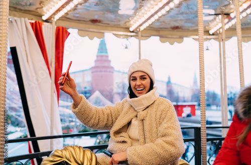 Smiling woman on illuminated carousel taking selfie on smartphone