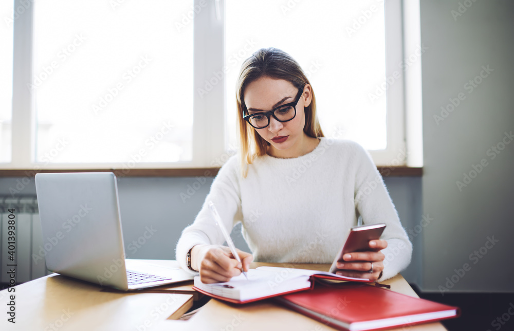 Female freelancer working on laptop and smartphone while making notes Female freelancer working on laptop and smartphone while making notes