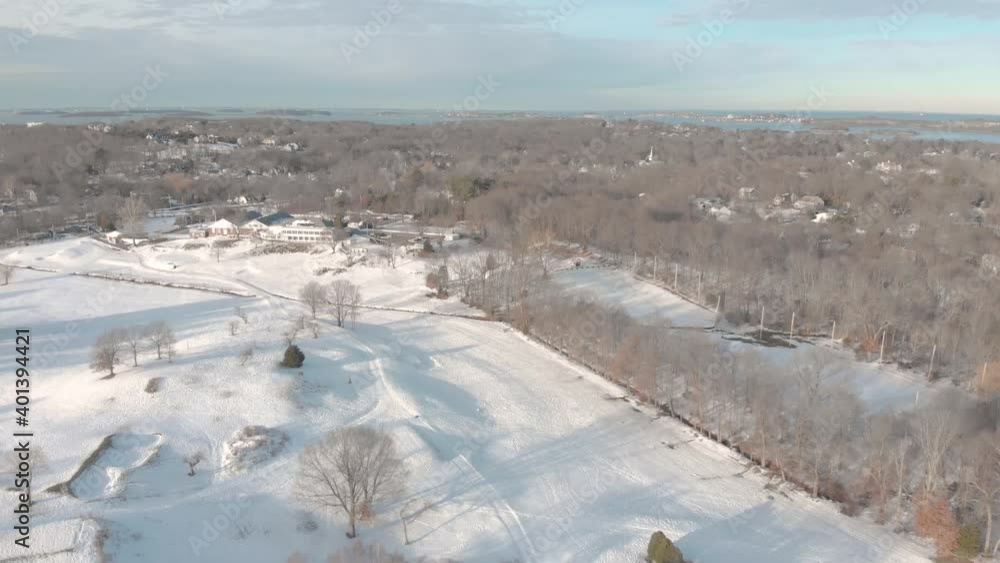 A short drone clip showing the harbor in the distance and a snow-covered country club below. Backing away shot revealing trees and more. A short drone clip showing the harbor in the distance and a snow-covered country club below. Backing away shot revealing trees and more.