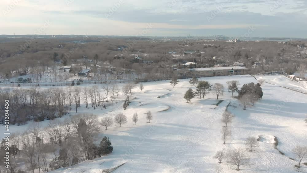 Gentle and slow drone aerial toward Boston in the distance, over a snowy golf course. Water in view. Gentle and slow drone aerial toward Boston in the distance, over a snowy golf course. Water in view.