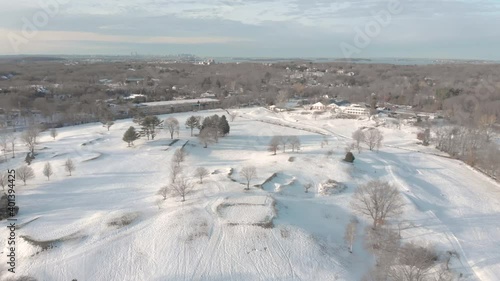 A leftward pan over a snowy golf course to reveal Boston, MA, USA on the horizon. Drone view with water and other features in the distance. photo