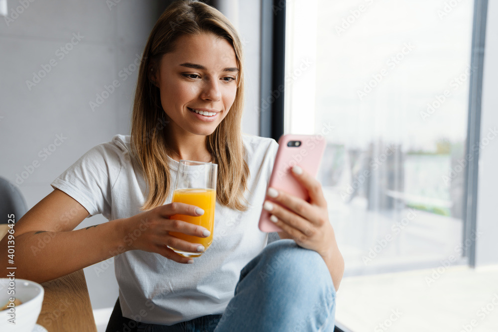 Beautiful happy girl using mobile phone while drinking juice Beautiful happy girl using mobile phone while drinking juice