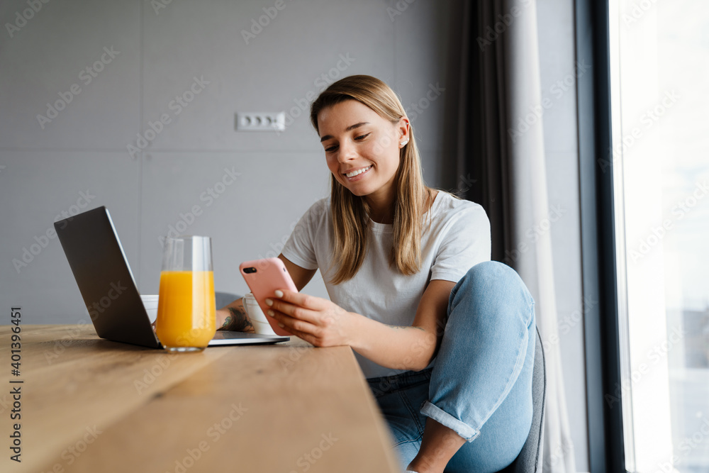 Happy girl using mobile phone and laptop while having breakfast Happy girl using mobile phone and laptop while having breakfast