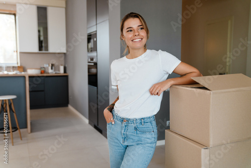 Beautiful girl smiling and standing by cardboard boxes in apartment