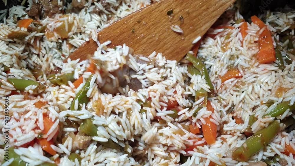 Female hand mixes with wooden spatula rice, vegetables, meat. Cooking pilaf . Multi-ethnic home cooking. Female hand mixes with wooden spatula rice, vegetables, meat. Cooking pilaf . Multi-ethnic home cooking.