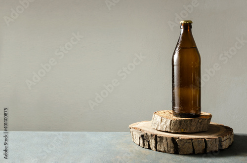 Brown glass bottle of cold and fresh drink on the wooden tray, grey table against grey wall.Empty space photo
