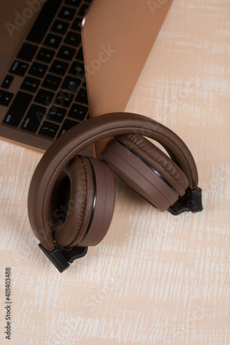 Fragment of an open pink laptop. Nearby are wireless headphones in brown. The surface is painted in white and beige.